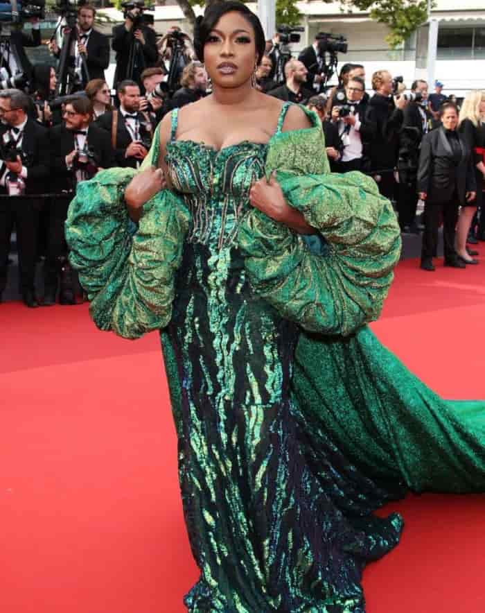 Chika Ike in an ornate green shimmering gown with a puff cape train