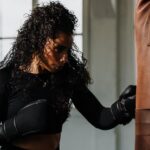 a woman in a black top and black gloves near a punching bag