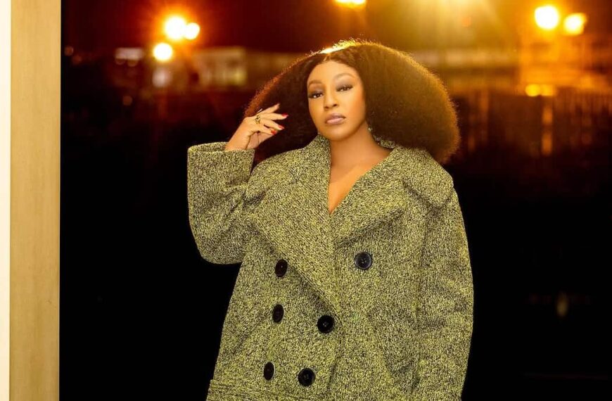 Fashion photo of Rita Dominic posing in a tweed jacket, green jacket, and platform shoes - Fashion Police Nigeria