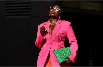 photo of a lady on a pink blazer, orange pants and carrying a green bag